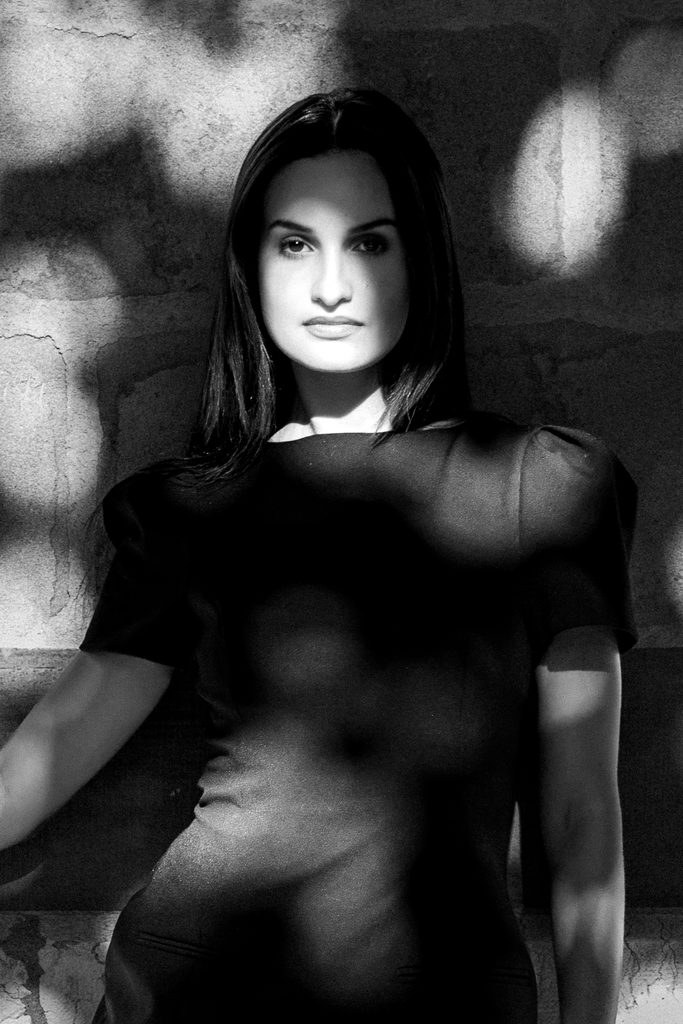 Portrait resserré d'une femme adossée au mur de la cathédrale Saint-Pierre, le visage émergeant des taches de lumière projetées par un arbre, Genève, noir et blanc
